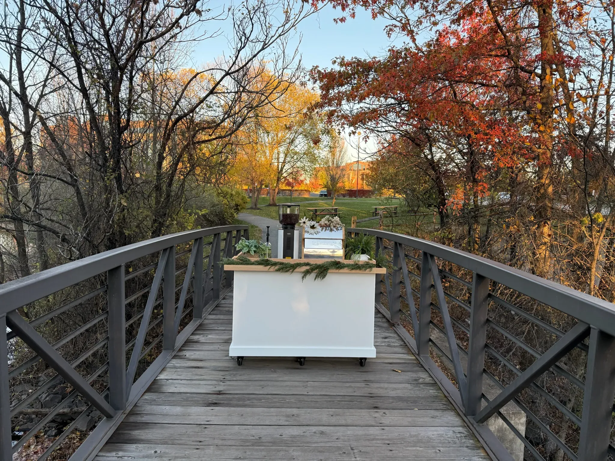 The Barnabas Coffee Co. espresso cart set up on a footbridge, an autumn lake behind it